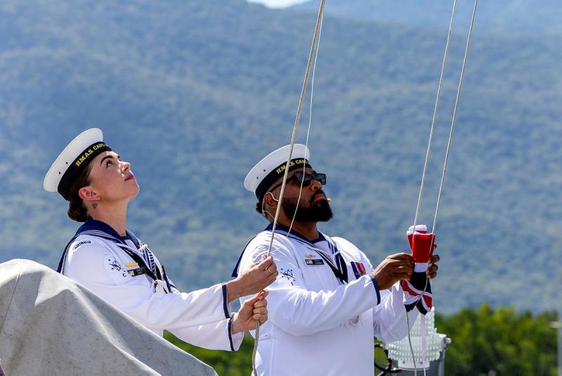 Two Navy members in white uniforms look up and pull on ropes.