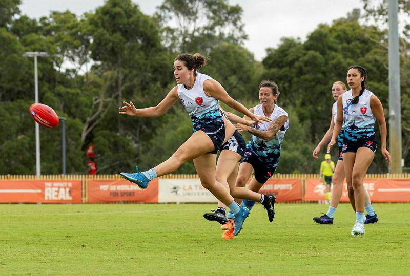 A female AFL player kicks the ball during a game.
