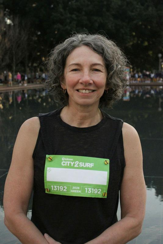 A woman before a body of water with a City2Surf tag on her shirt.