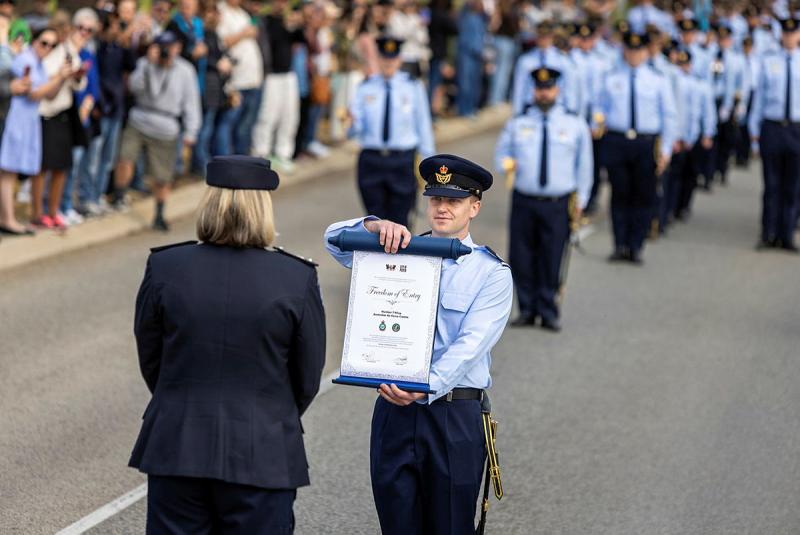 A military member shows a scroll reading 'Freedom of Entry' to a military woman with her back to the camera.