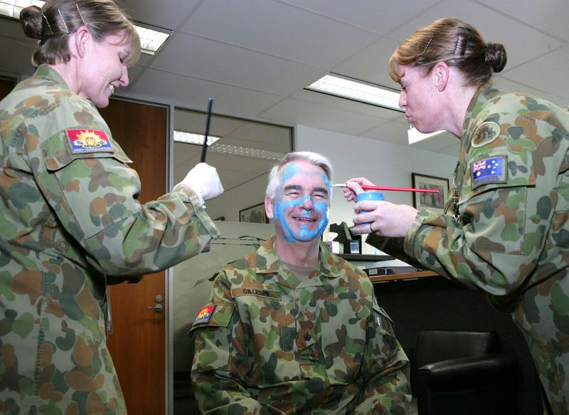 Two Army women paint the face of an Army man.