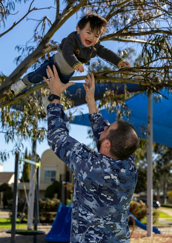 A military man throws a laughing child up into the air.