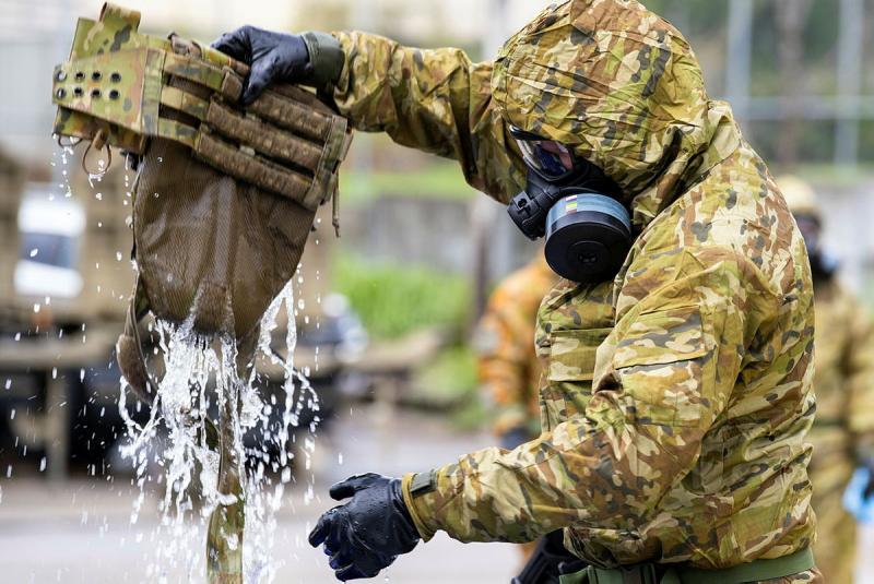 A person in a hazmat suit holds up a bag with water streaming from it.