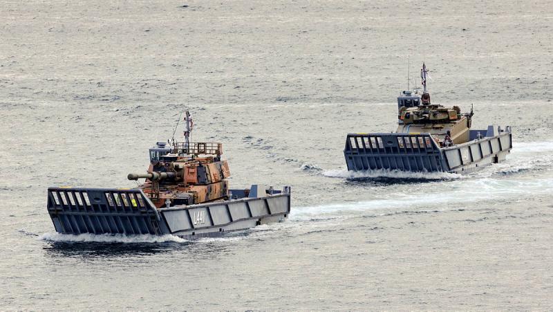 Two vessels carry armoured vehicles across the water.