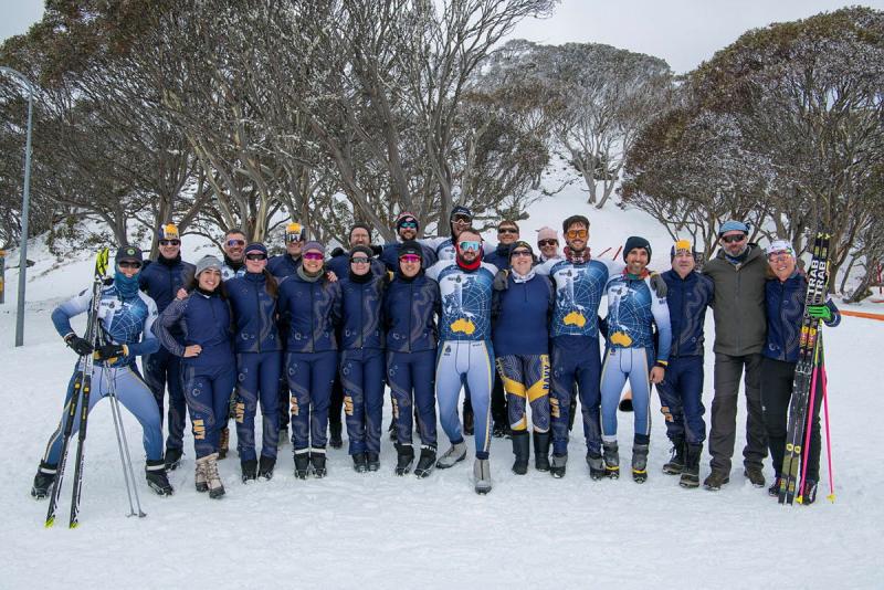 A large group of people in snow gear and with skis stand in a snowy forest.
