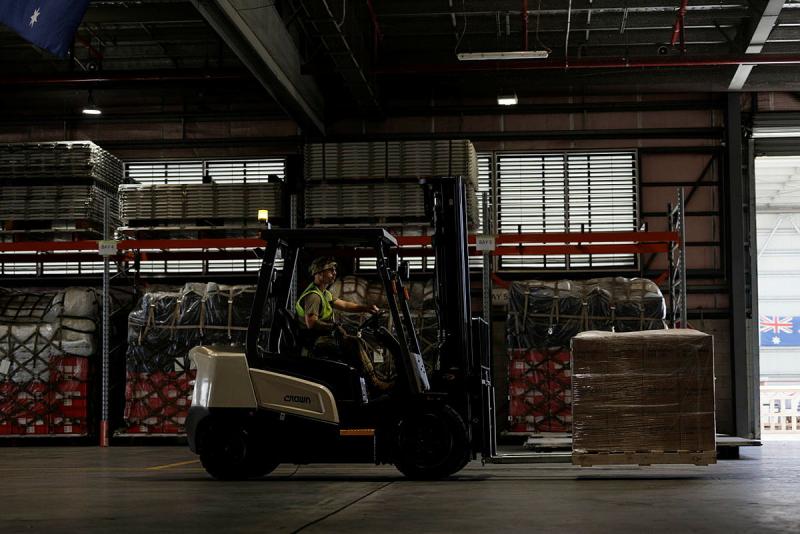 A man in high-vis transports a large wrapped box on a small forklift.