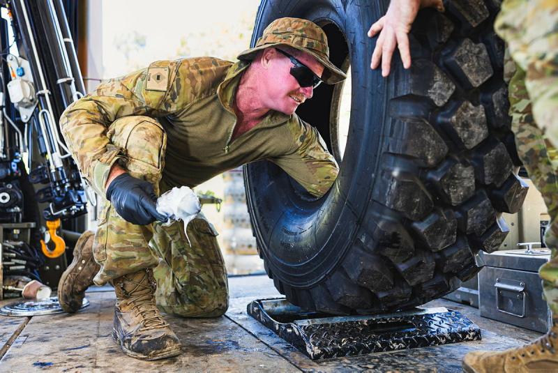 An Australian Army soldier kneeling down, applies lubricant to the inside of a vehicle tyre in preparation for fitting.