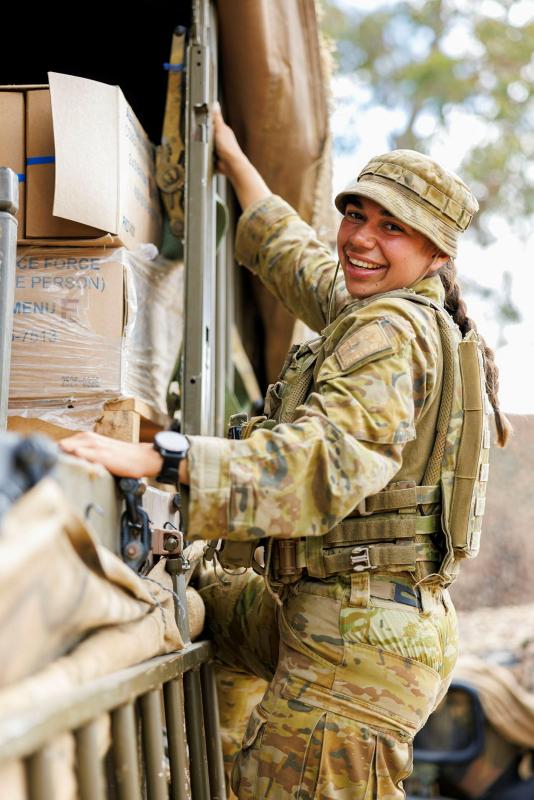 A soldier holds on to the side of an area full of supplies in cardboard boxes.