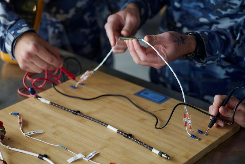 A close up of several military members working on a wiring board.