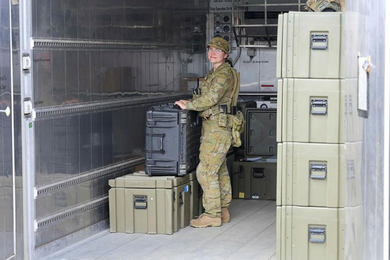 An Army member stands with large containers in a metal room.