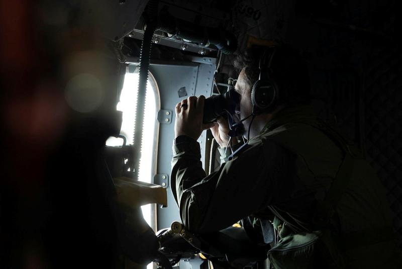 A man looks out the window of an aircraft with binoculars.