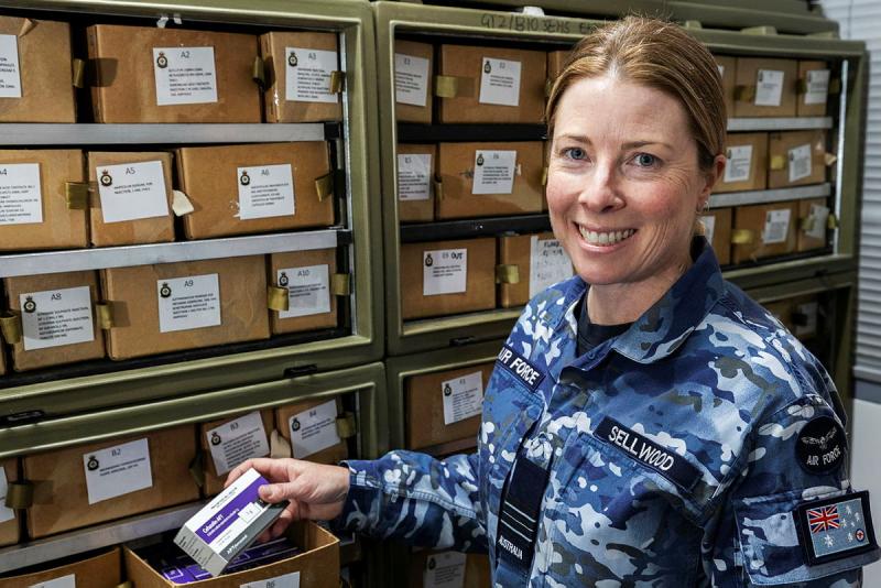 A woman in Air Force uniform stands holding a small box with writing on its label.