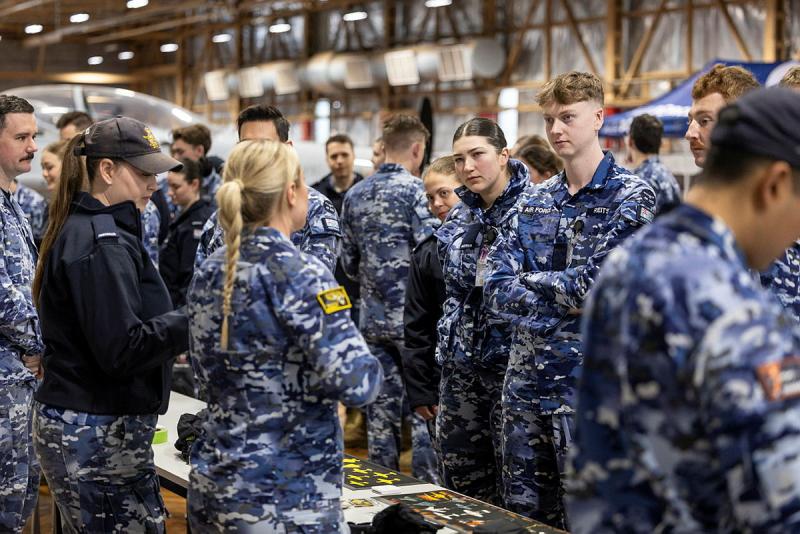 A large group of military personnel approach an information table run by other military personnel.