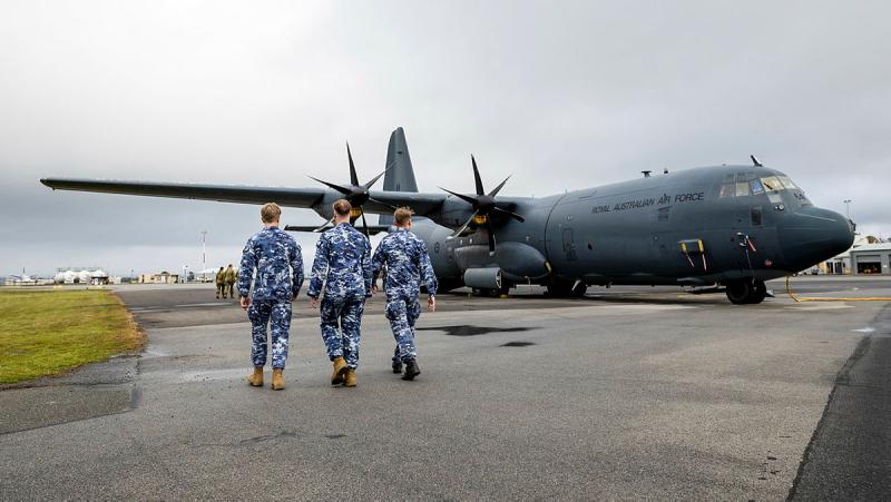 Three men in military uniform walk towards a stationary aircraft.