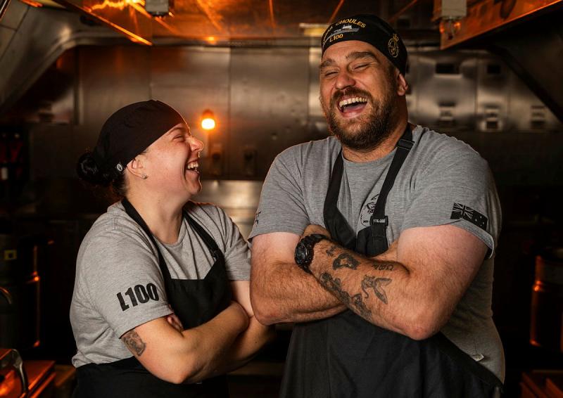 Two chefs laugh together in a kitchen.
