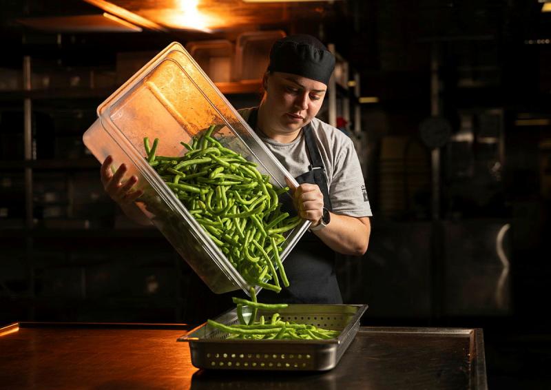 A chef pours beans from a large white tub in a dimly lit room.