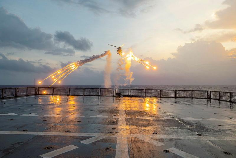 A helicopter fires flares behind a ship.