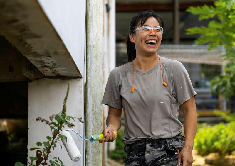 A sailor holds a paint roller and smiles.