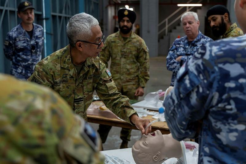 Army and Air Force personnel stand around a mock operating table with a rubber dummy playing an injured soldier.