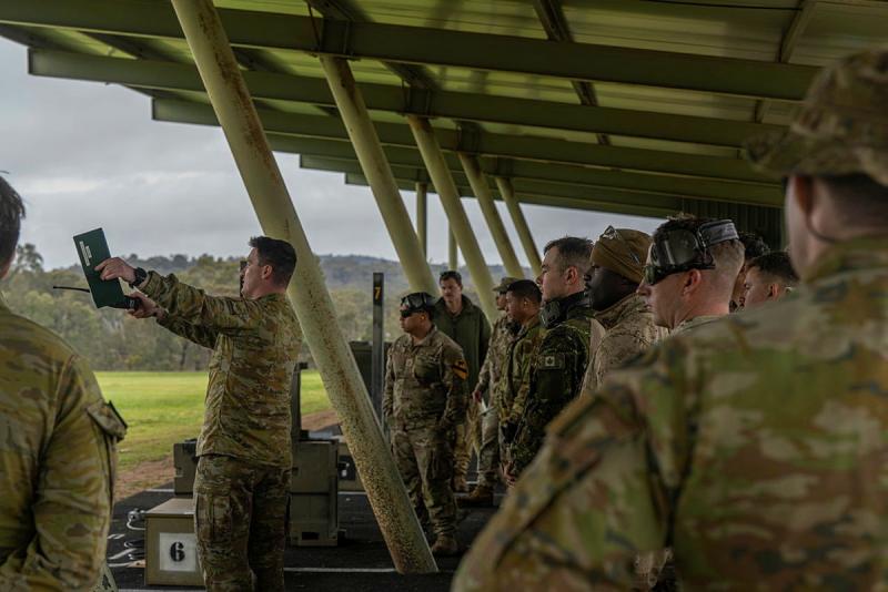 A group of military personnel, all looking in the same direction, stand under a shelter.