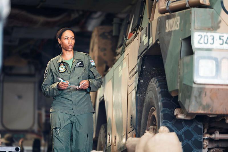 An Air Force member walks beside an Army truck with pen and paper in hand.