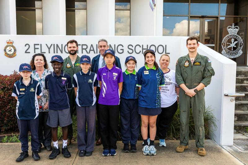 Two military men stand with civilian adults and children in front of a flying training school.