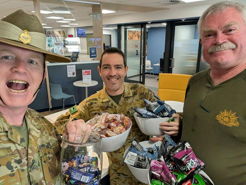 Three soldiers gather together and hold up bowls of sweet treats.