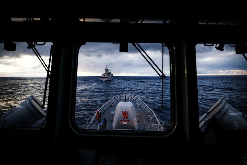 The ocean and a ship in the distance are seen through the front windows of a ship.