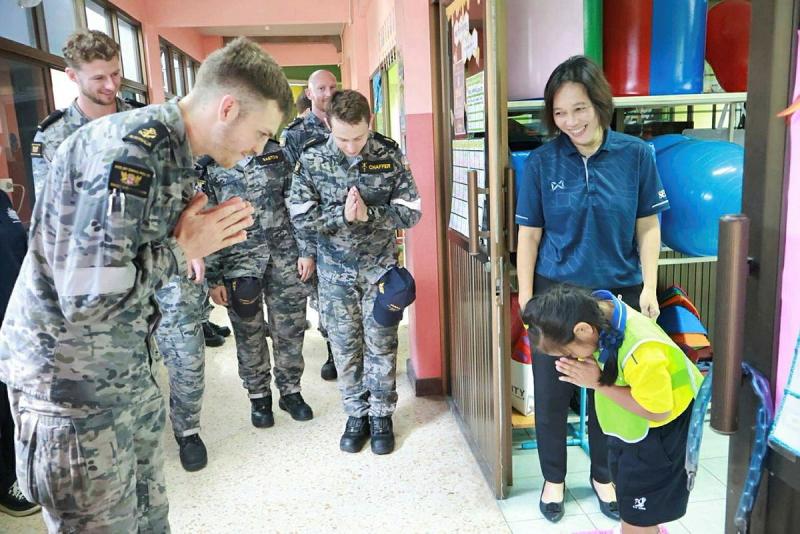 Navy personnel bow with their hands in a prayer position to a young school student who bows back to them.