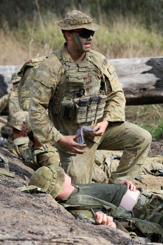 A military man speaks above another military member laying down with a hand on his abdomen.