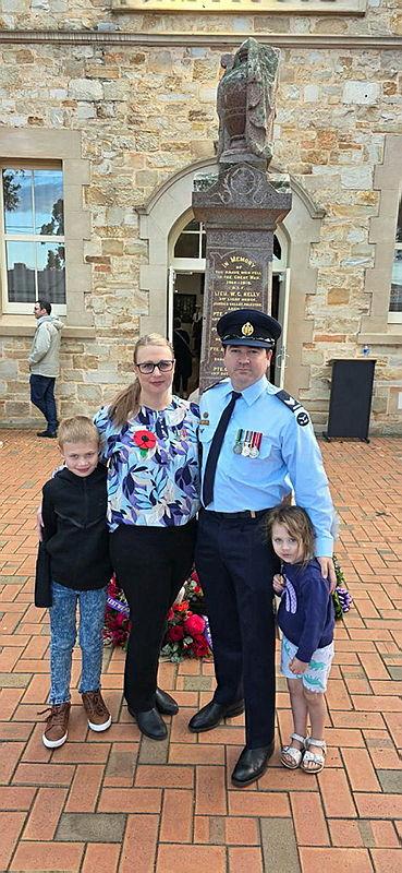 A man in ceremonial dress and his family pose for a photo in front of a statue.