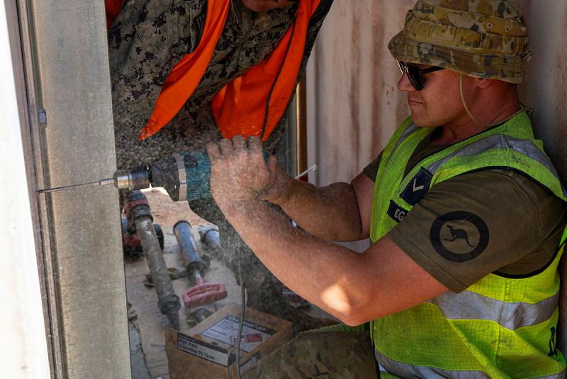 A military man in high-vis uses a drill.