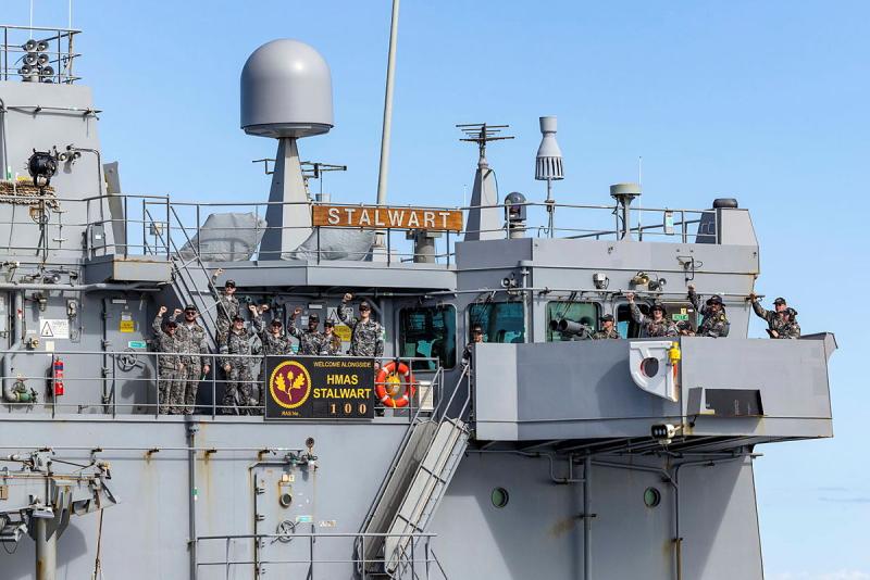 Navy personnel stand on a ship and wave.