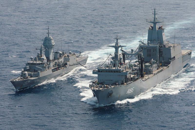 Two ships sail side by side linked by a fuel line.