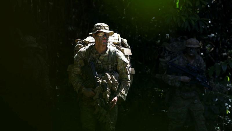 Several armed military personnel emerge from the bush, one stepping directly into the light.