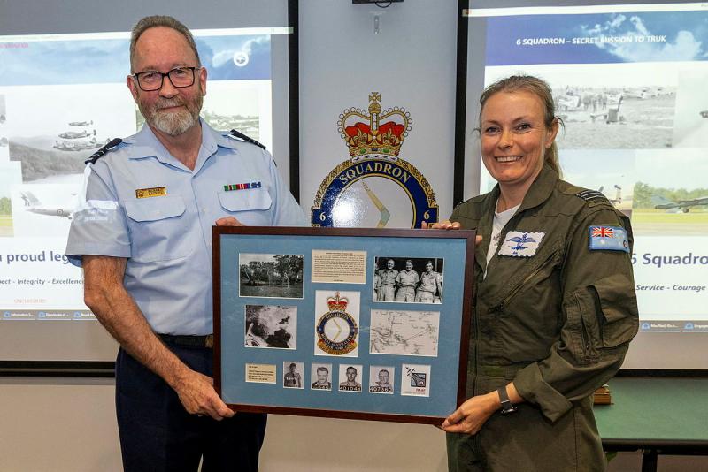 Two military personnel hold up a plaque with old pictures and text.