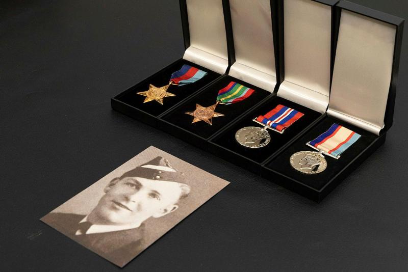 A black and white photo of a military member sits next to four medals in their boxes.