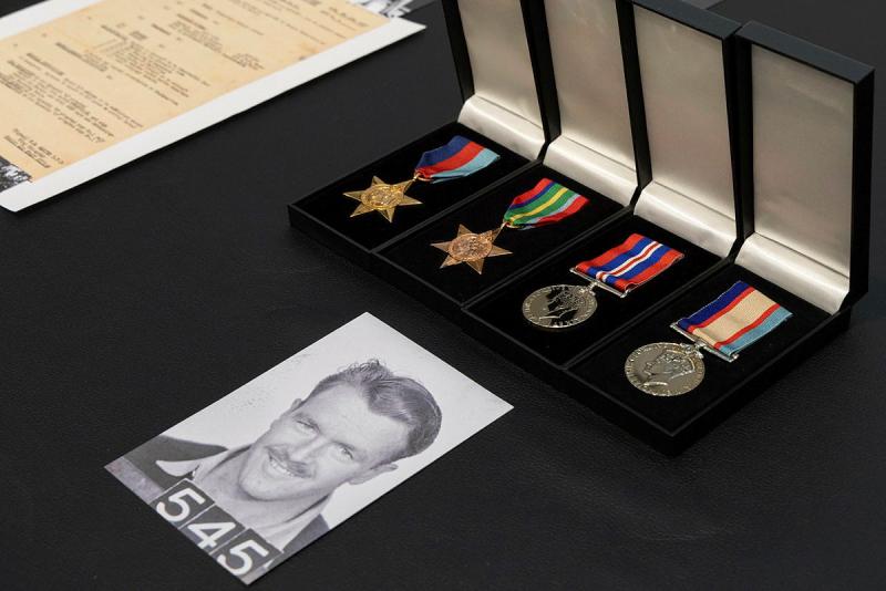 A black and white photo of a military member sits next to four medals in their boxes.