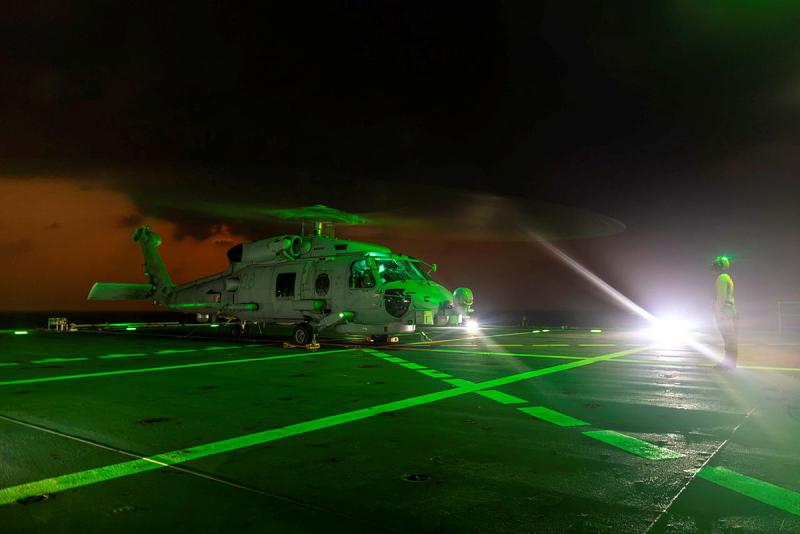 A helicopter lands on a ship during the night.