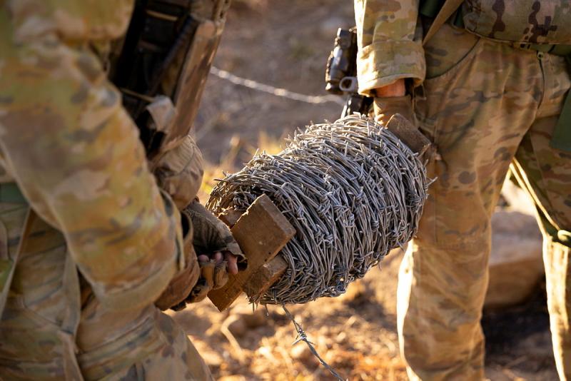 Two military members carry a roll of barbed wire.