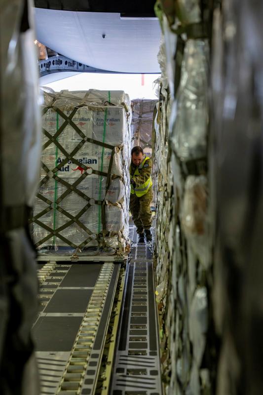 A military man in high-vis pushes a large pallet of Australian Aid into the belly of a vehicle.