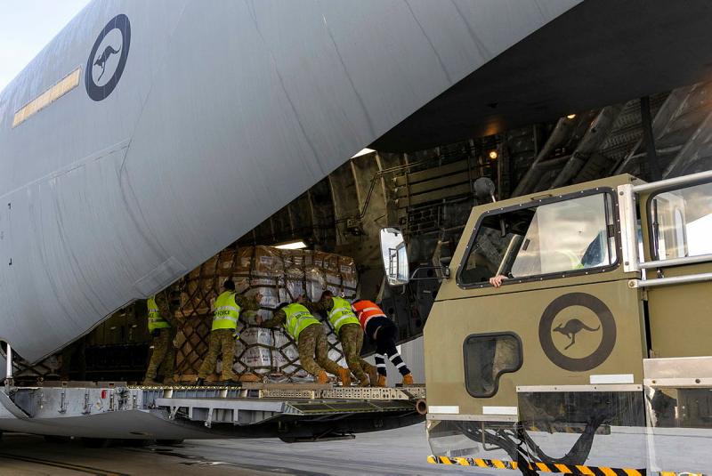 Several military members in high-vis push a large pallet into the belly of an aircraft.