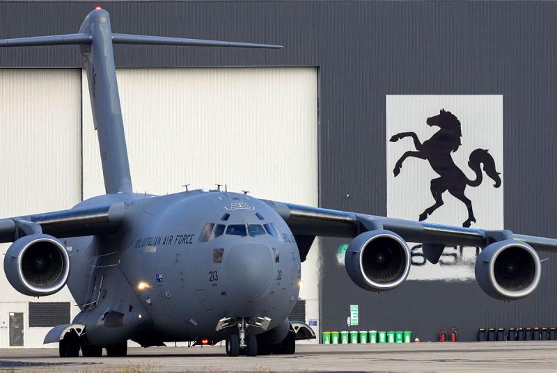 An aircraft readies to take off from the ground near a warehouse building.