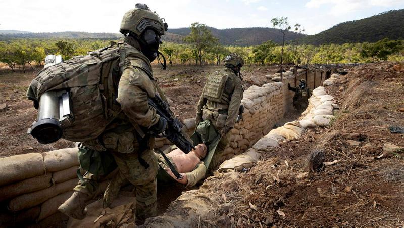 Two soldiers carry a fake casualty through a trench.