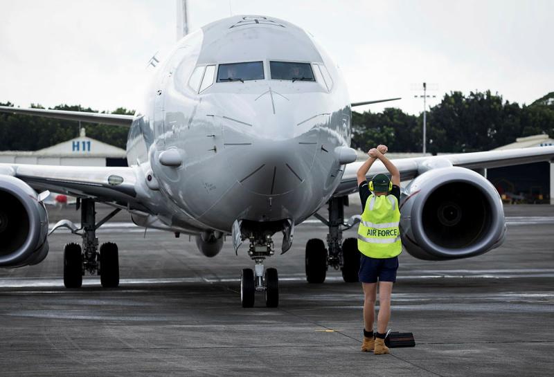 An Air force member stands in front of a large aircraft with his hands above his head and crossed over at the wrist.