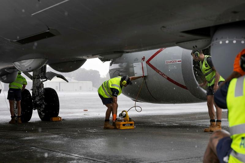 Workers in bright yellow clothing inspect the underside of an aircraft.