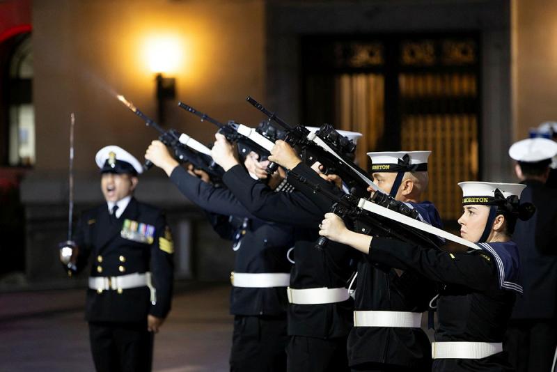People in black and white uniforms fire weapons towards a darkened sky.