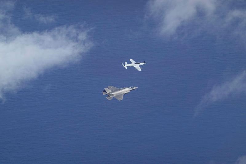Two different aircraft fly close together in a blue sky. 