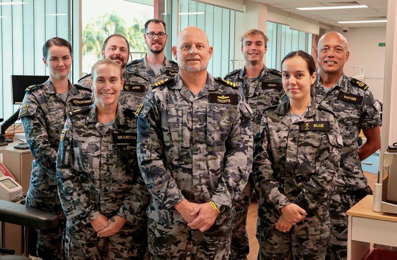 A group of Navy personnel in uniform stand smiling for the camera.
