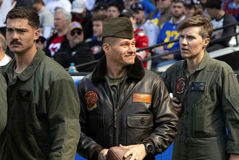 Three military men walk past a seated crowd.